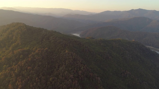 空中拍摄的绿树在山上的森林日落，无人机飞向河流对天空-湄公河，老挝视频素材