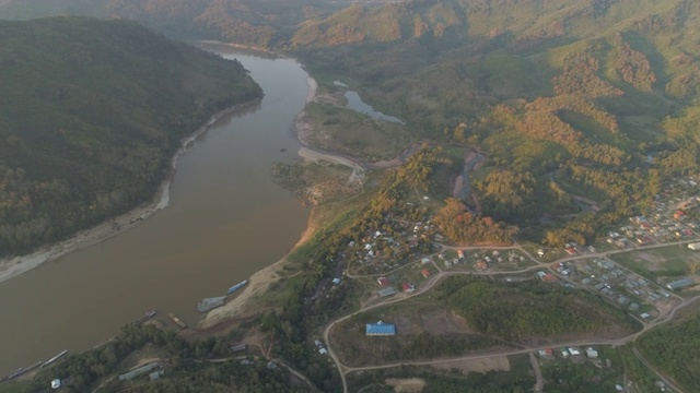 空中拍摄的房子附近的河流在日落，无人机飞行平移山脉对天空-湄公河，老挝视频素材