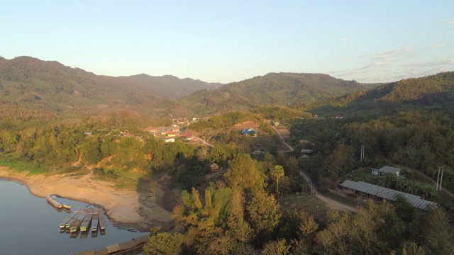 航拍停泊在河岸附近的树木和村庄的船只，无人机在天空的映衬下飞越河流——老挝湄公河视频素材