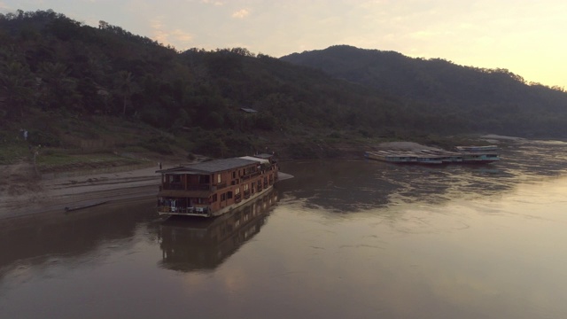 航拍邮轮停泊在河岸在日落，无人机在森林附近的树木-湄公河，老挝视频素材