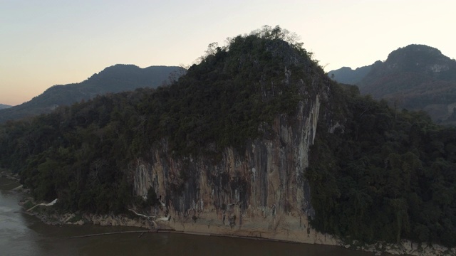 空中拍摄的树木在河流附近的悬崖上的天空，无人机向后飞行在日落-湄公河，老挝视频素材