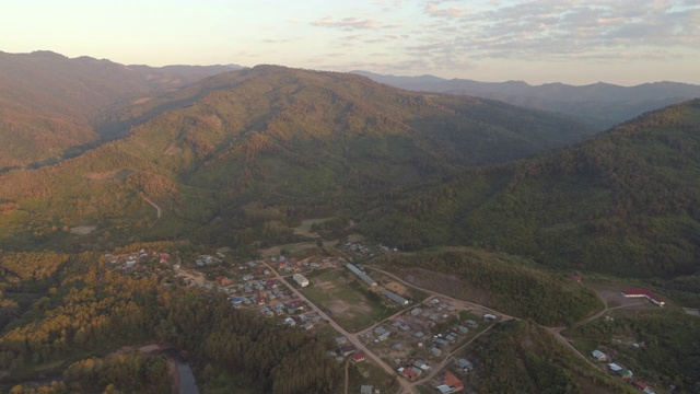 空中拍摄的房子在树林中的村庄在日落，无人机向前飞行的住宅建筑周围的山对天空-湄公河，老挝视频素材