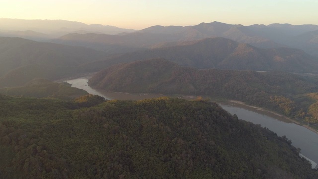 空中拍摄的绿树在山上的森林在日落，无人机平移附近的河流对天空-湄公河，老挝视频素材