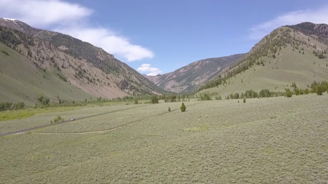 空中平移拍摄美丽的绿色山谷对天空，无人机飞过风景与汽车行驶在乡村道路在阳光明媚的一天-博伊西，爱达荷州视频素材