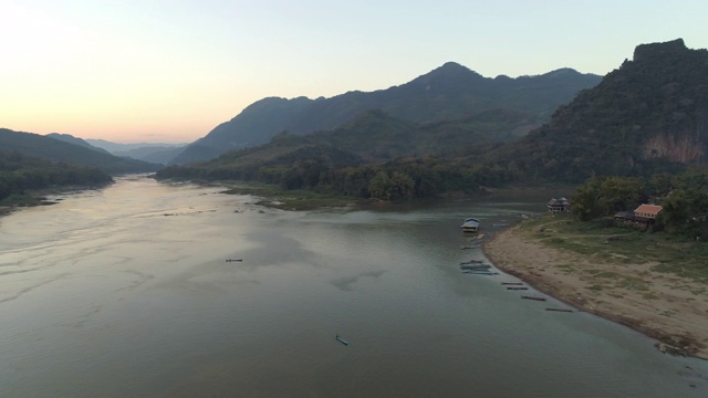 空中拍摄的船只停泊在河岸附近的村庄，在日落时无人机在山脉上平移-湄公河，老挝视频素材