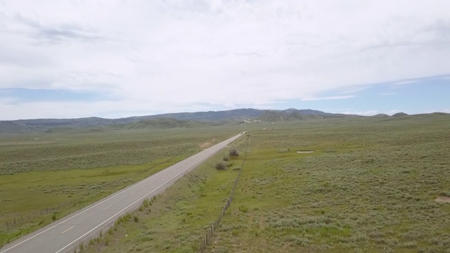 空中平移拍摄在多云的天空下乡村道路上行驶的车辆，无人机向后飞行在绿色景观-博伊西，爱达荷州视频素材