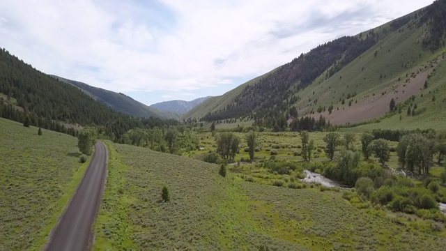 空中拍摄的空的乡村道路附近的河流对山脉，无人机飞向前，而平移在阳光明媚的一天-博伊西，爱达荷州视频素材