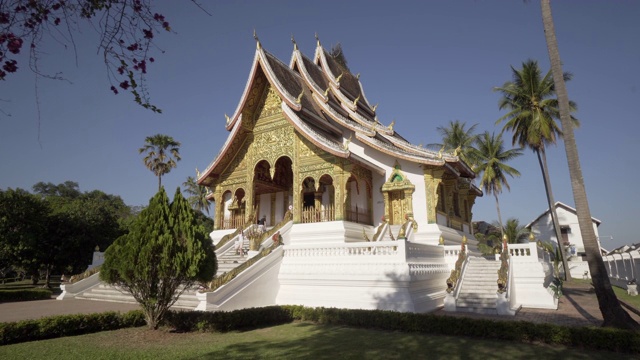 在阳光明媚的日子里，游客在著名的Phra Bang寺庙中棕榈树对着天空的镜头——琅帕邦，老挝视频素材