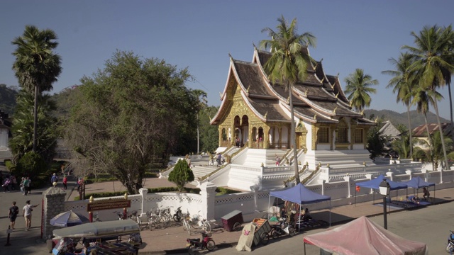 在阳光明媚的日子里，镜头拍摄的是游客在城市街道旁的著名的Phra Bang寺庙，老挝的Luang Phabang视频素材