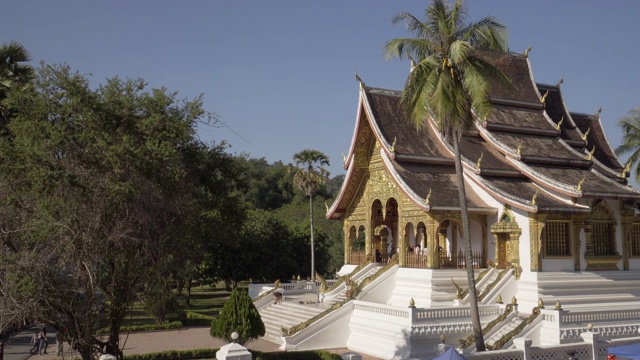 在阳光明媚的日子里，游客在著名的Phra Bang寺庙中对着天空的树木-琅法邦，老挝视频素材