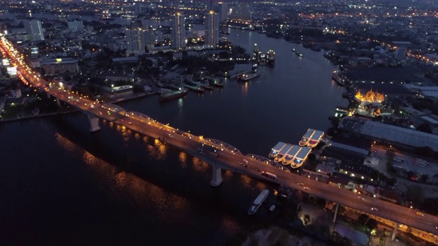 空中倾斜拍摄的车辆在黄昏的城市河上照亮桥梁，无人机在城市上空飞行-曼谷，泰国视频素材