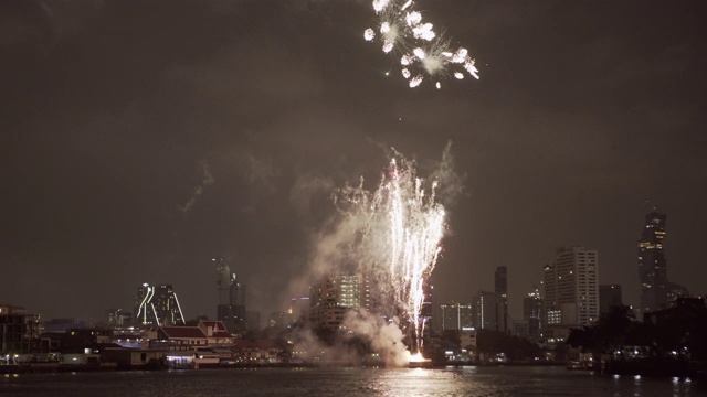 泰国曼谷，夜晚在河边的天空映衬下，烟火在建筑物上空爆炸并伴随着烟雾视频素材