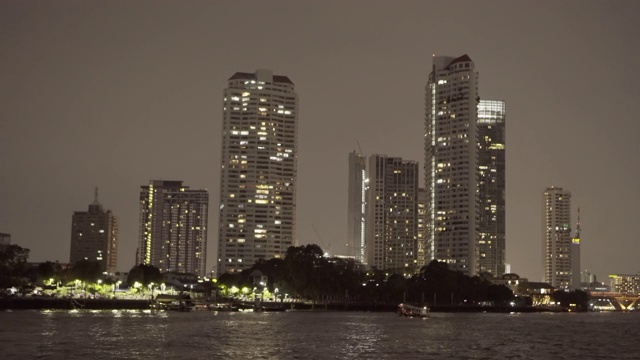 在曼谷，泰国的夜晚，灯光照亮的现代摩天大楼在城市的河流对天空视频素材