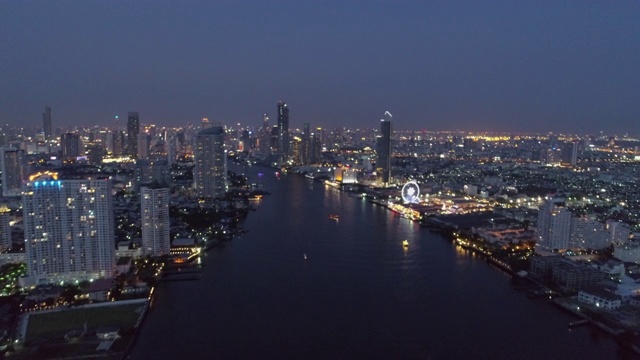 航拍的河流在城市的建筑物照亮，无人机向前飞行的城市景观在夜晚的天空-曼谷，泰国视频素材