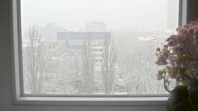 城市公寓窗外突然下起雪。白色的蓬松的雪覆盖了广场，街道和房子的城市景观。视频素材