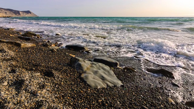 时光流逝——波浪翻滚在一幅卵石的海景上，背景是一座山视频素材