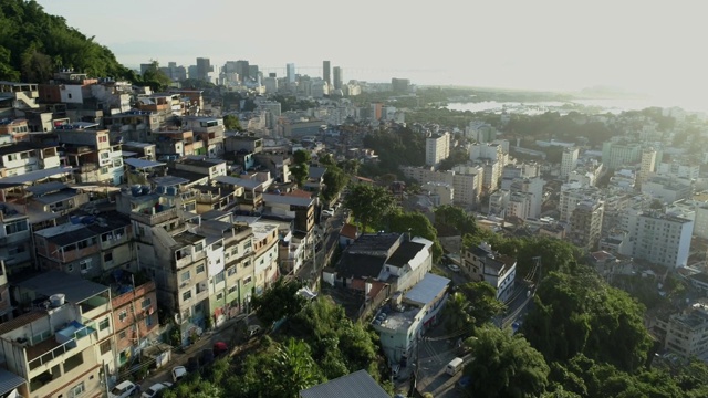 日出高空飞过山顶贫民窟，背景是里约热内卢市中心的高楼大厦视频素材