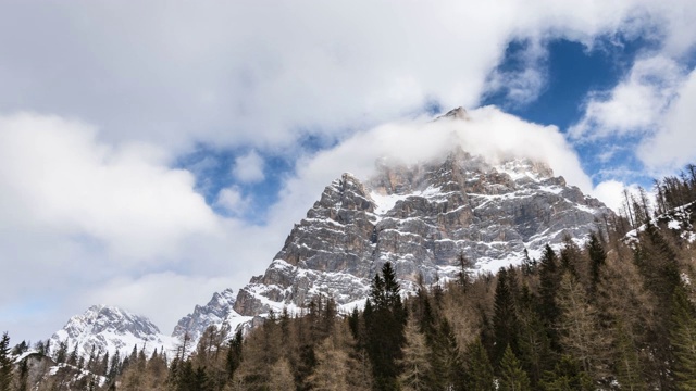 在冬季，欧洲阿尔卑斯山脉的积雪覆盖的岩石山峰上方移动云的延时视频素材