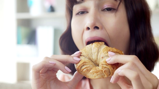 年轻女子咬着吃一个美味的大羊角面包视频素材