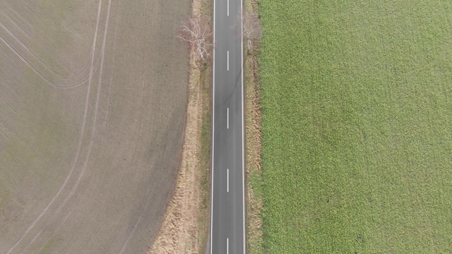 在德国北部孤独而空旷的小乡村公路上，沿着空旷的公路飞行在60米的高度，用无人机鸟瞰视频素材