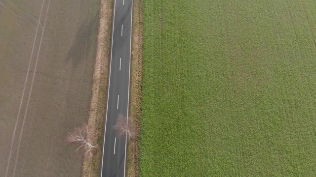 在德国北部，两辆车行驶在一条荒凉的小乡村道路上，在60米的高空飞行在空旷的道路上，无人机的鸟瞰图，在镜头的最后上升视频素材