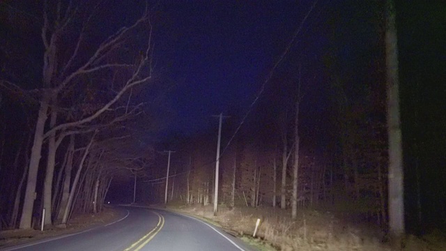 在乡村的高速公路上行驶，穿过山林，在夜晚。驶近的汽车前灯使司机失明。视频素材