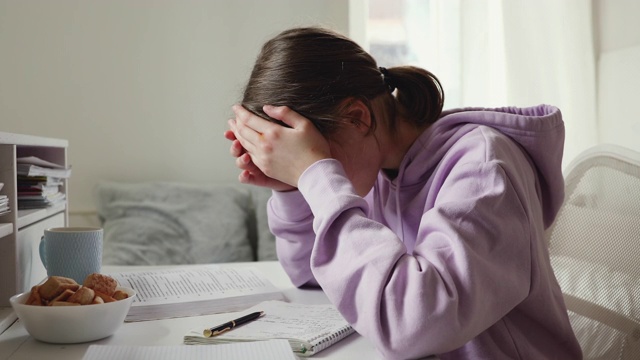 疲惫不安的女学生独自学习，在家里感到头痛视频素材