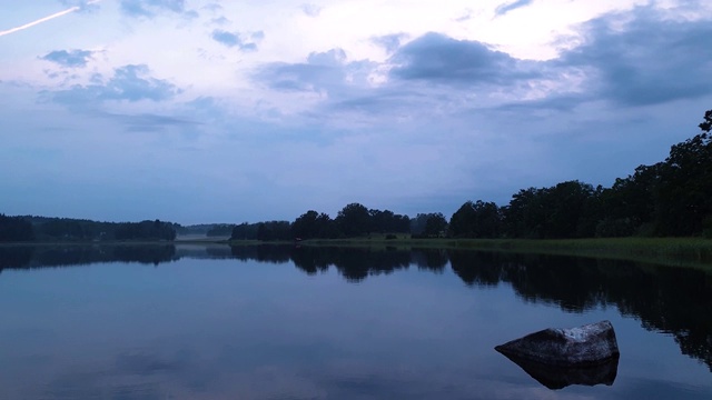 美丽的日落在平静的夏夜。湖岸与绿色的树木和植物反射在水晶干净镜面水面。天空乌云密布。缓慢的运动。视频素材