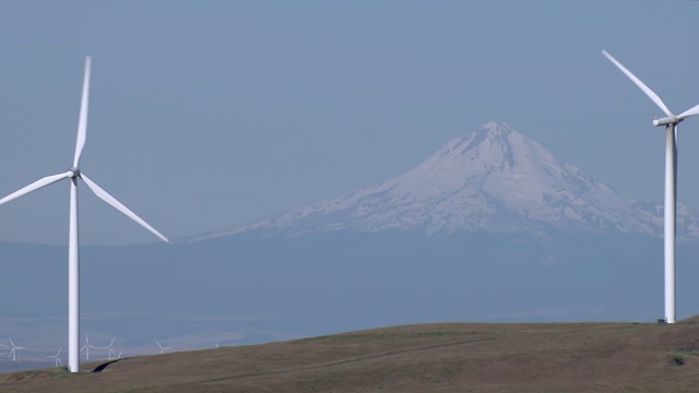 风力涡轮机在俄勒冈州积雪覆盖的胡德山前旋转的鸟瞰图。视频素材