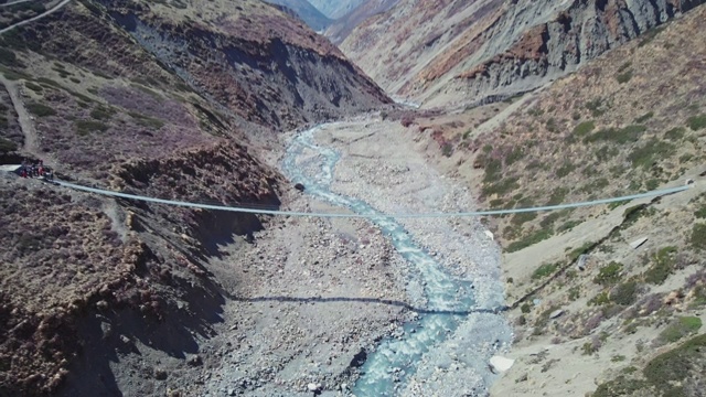 悬索桥悬挂在岩石河峡谷上，映衬着雪山全景视频素材