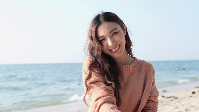 亚洲美丽的少女快乐和微笑在海边的海滩夏天。一个女人抓起一把干沙子，让它掉下来。视频素材