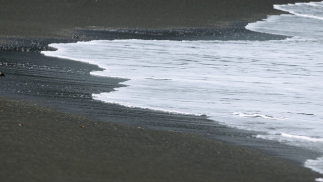 缓慢运动的波浪滚过火山沙视频素材