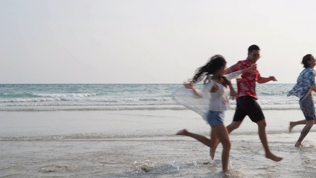 亚洲十几岁的男孩和女孩快乐地在海边海滩夏天跑步。年轻的亚洲玩跑步乐趣和周年庆典。4K分辨率和慢镜头。视频素材