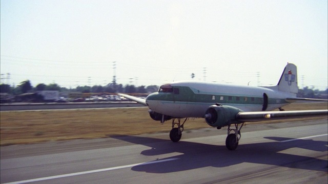 在小镇的跑道上看到商业建筑和主要街道在bg dc-3白色和绿色/相机移动和平移/飞机出租车/转身起飞/飞机视频素材