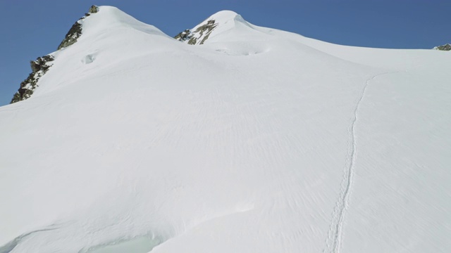 登山运动员的足迹穿过白雪覆盖的斜坡，一直延伸到山顶视频素材