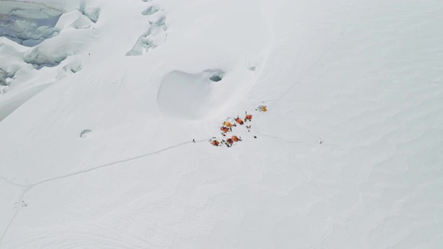 空中降落在宽阔闪亮的雪原上，登山者帐篷营地的上方视频素材