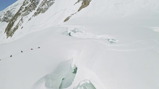 登山者们在一个宽阔的山坡上休息，旁边是一个巨大的坍塌的雪洞视频素材