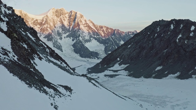 日出时，在广阔的雪原上，巨大的岩石山脉上，空中飞过高山营地视频素材