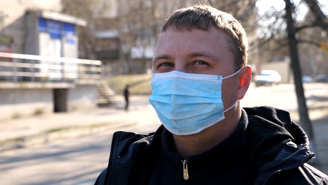 新冠肺炎疫情期间，佩戴医用口罩的男子站在城市街道上。戴着防护口罩的人。应对冠状病毒大流行的健康和安全生命理念。视频素材