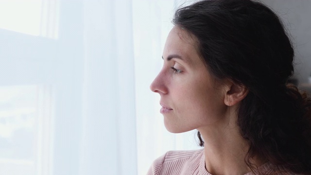 愁眉苦脸的年轻成年女子望着窗外视频素材