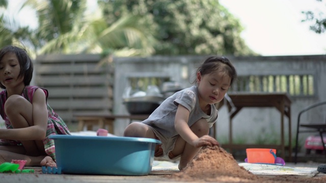 两个亚洲小女孩在院子里玩沙子玩得很开心。真实生活，手持拍摄视频下载