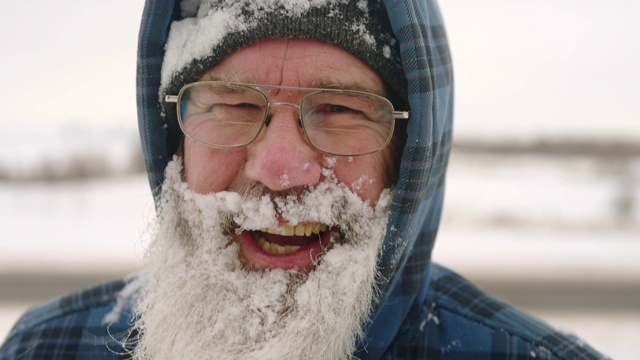 成熟的大胡子男人在冬天的外面笑着，脸上挂着雪。视频素材