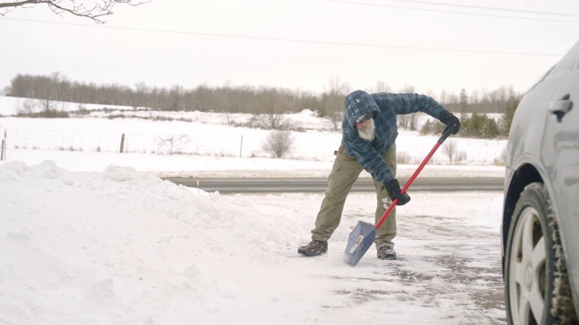 一个成熟的男人在一场冬季降雪后铲他的车道。视频素材