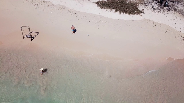 一对夫妇在印度尼西亚龙目岛的粉红色海滩上玩耍。波浪轻轻地拍打着海岸。女孩在戏水，男人在玩无人机。快乐和粗心的时刻。视频素材