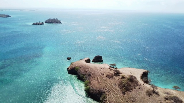 一架无人机在印度尼西亚龙目岛田园诗般的粉色海滩附近的海岬上空飞行。海是平静的，闪烁着许多深浅不一的蓝色，温柔地冲刷着悬崖。大自然的美。未遭破坏的,隐藏的宝石视频素材