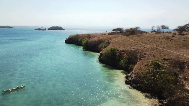 一架无人机在印度尼西亚龙目岛田园诗般的粉色海滩附近的海岬上空飞行。海是平静的，闪烁着许多深浅不一的蓝色，温柔地冲刷着悬崖。大自然的美。未遭破坏的,隐藏的宝石视频素材