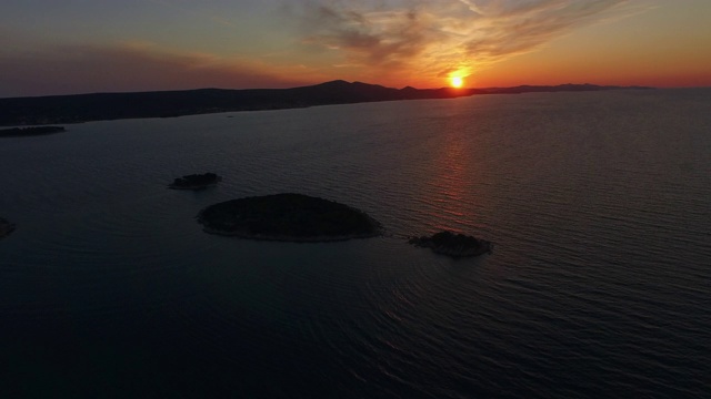 空中平移拍摄在日落的天空在海上的小岛屿，无人机飞过美丽的自然景观-心岛，克罗地亚视频素材