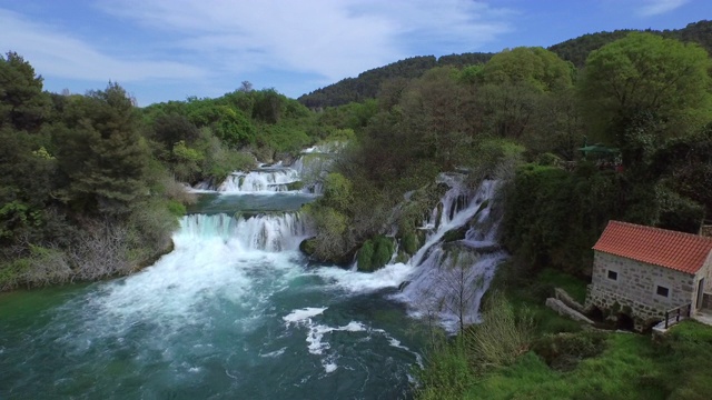 空中拍摄的美丽瀑布的建筑对天空，无人机飞向瀑布在树木中- Krka，克罗地亚视频素材