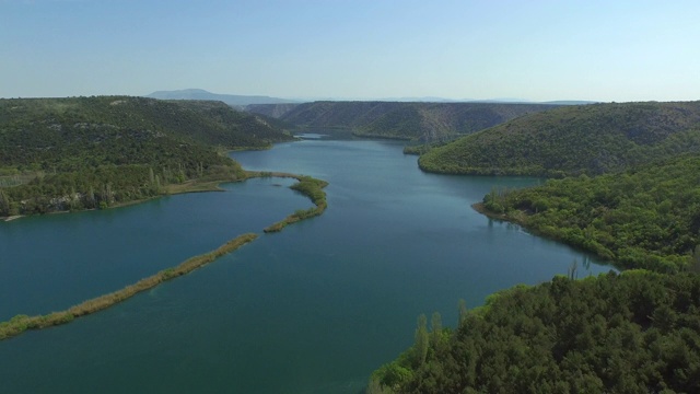 空中拍摄的美丽的河流在绿色的山脉与天空，无人机正在后退- Krka，克罗地亚视频素材