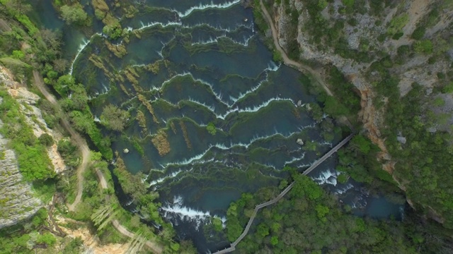 从空中拍摄河流在长满绿色植物的岩石山中流动，无人机在克罗地亚的克尔卡山谷上空飞行视频素材